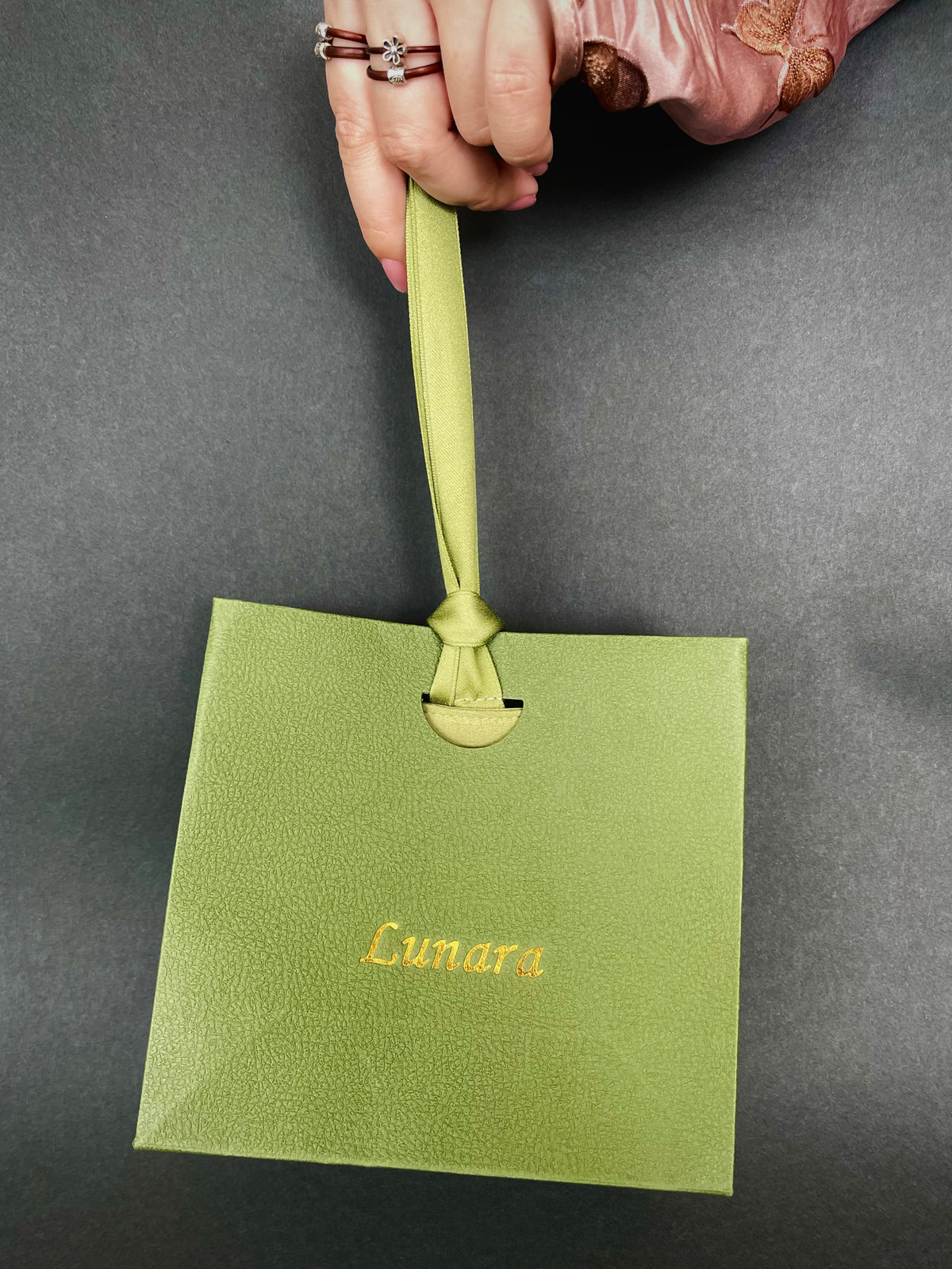 Hand holding a sage green Lunara gift bag